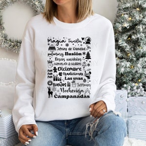 May include: White sweatshirt with a black design featuring a Christmas-themed word cloud in Spanish. The words include "Magia", "Familia", "Jersey de Navidad", "Ilusion", "Deseos Navideños", "Chocolate & Churros", "Diciembre", "Tradiciones", "Las uvas", "Sueños", "Turrones", "Nochevieja", and "Campanadas".