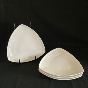 May include: Two white triangular ceramic plates. The top plate is on a black stand. The bottom plate is stacked on top of two other plates.