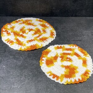 May include: Two crocheted pot holders in a spiral pattern with white and orange yarn.