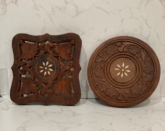 May include: Two intricately carved wooden coasters with floral designs. The coasters are brown with a white inlay in the center of each.