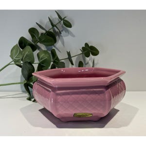 May include: A hexagonal pink ceramic planter featuring a raised diamond-quilted texture on its exterior sides. The planter has a smooth, glossy finish and includes a small rectangular gold-colored label on the front with the text Hagen-Renaker.