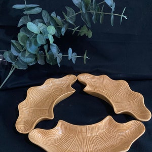 May include: Three ceramic serving dishes in a light brown color. The dishes are shaped like a crescent moon and have a textured surface that resembles woven wicker.