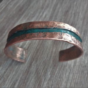 May include: Copper cuff bracelet with a hammered texture and a turquoise inlay. The open design allows for easy wear. The bracelet's warm copper tones contrast with the cool turquoise, creating a striking accessory.
