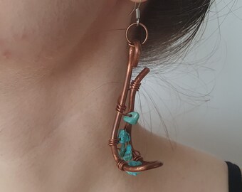 May include: Copper wire earrings with turquoise stone accents. The earrings have a curved design with turquoise stones clustered at the bottom. The ear wires are silver-coloured.