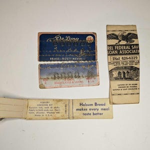 May include: A collection of vintage advertisements, including a De Long Hooks, Eyes & Loons advertisement, a Holsum Bread advertisement, and a  Rel Federal Savings & Loan Association advertisement. The De Long advertisement features a blue and white design with the text "De Long" and "BRASS-RUST? NEVER!!". The Holsum Bread advertisement features a white background with the text "Holsum Bread makes every meal taste better". The Rel Federal Savings & Loan Association advertisement features a black and white design with the text "Rel Federal Savings & Loan Association" and "Dial 426-6319".