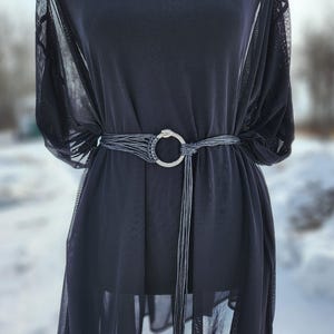 Op de afbeelding: Een zwarte, doorschijnende jurk met een zwarte leren riem met een zilveren slangenringgesp.