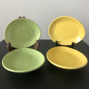 May include: Four ceramic plates, two green and two yellow, with a floral pattern. The plates are oval shaped and have a slightly raised rim.