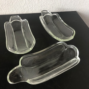 May include: Three clear glass dishes in the shape of a banana. The dishes are on a black surface.