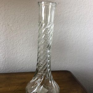 May include: A clear glass vase with a twisted design. The vase has a narrow neck and a wide base.