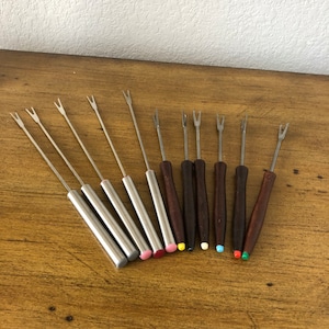 May include: Set of ten fondue forks with wooden handles and colorful tips. The forks are made of stainless steel and have a three-prong design.