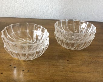 May include: Two stacks of clear glass bowls with a spiral design. The bowls are on a wooden surface. The bowls have a decorative, ridged pattern around the exterior. The bowls are likely for serving or display.