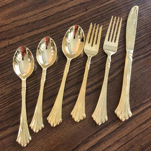 May include: Set of six gold-plated flatware, including two spoons, two forks, and a knife. The flatware has a decorative, fluted design.