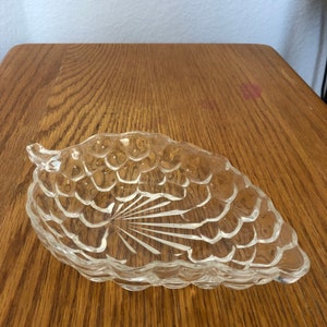 May include: A clear glass grape-shaped dish with a textured surface. The dish is designed to resemble a bunch of grapes.