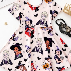 May include: A short-sleeved dress with a light pink background featuring a repeating pattern of cartoon characters dressed as witches, pumpkins, bats, and stars. The dress has a round neckline and a flared skirt. A sign reads rebel HOUSE.