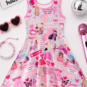 May include: A sleeveless skater dress with a light gray background featuring a collage of pink and red graphics, including hearts, butterflies, smiley faces, and text like 'Taylor's Version' and 'It's me, hi'. Accessories include heart-shaped sunglasses, a beaded bracelet, a disco ball, and a pink microphone.