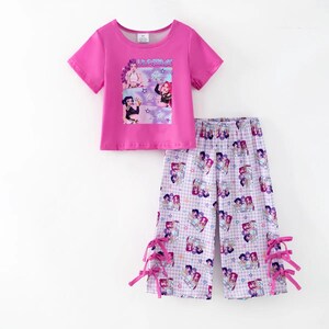 May include: A two-piece pajama set in bright pink. The short-sleeved top features a graphic with the text "HUNIRA" and images of cartoon characters. The pants are patterned with the same characters and have pink bows at the ankles.