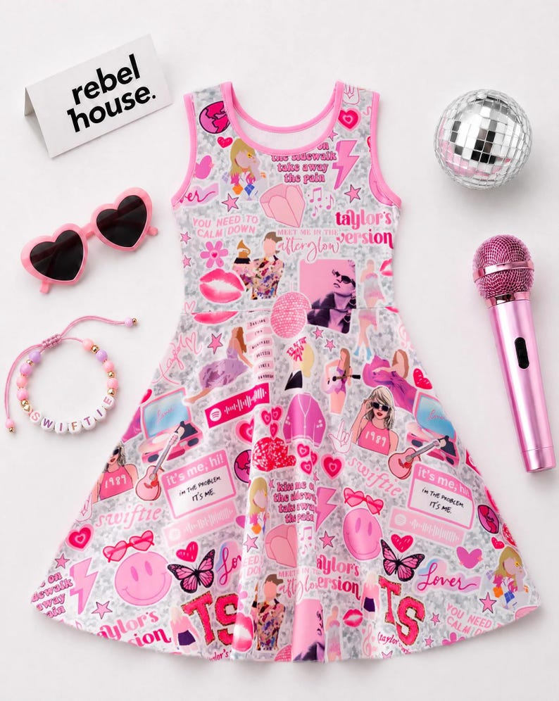 May include: A sleeveless skater dress with a light gray background featuring a collage of pink and red graphics, including hearts, butterflies, smiley faces, and text like 'Taylor's Version' and 'It's me, hi'. Accessories include heart-shaped sunglasses, a beaded bracelet, a disco ball, and a pink microphone.
