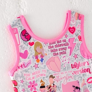 May include: A sleeveless top with a bright pink trim featuring a white and gray patterned background covered in various pink and colorful stickers, including text that reads Kiss me on the sidewalk take away the pain, You need to calm down, and Taylor's version.