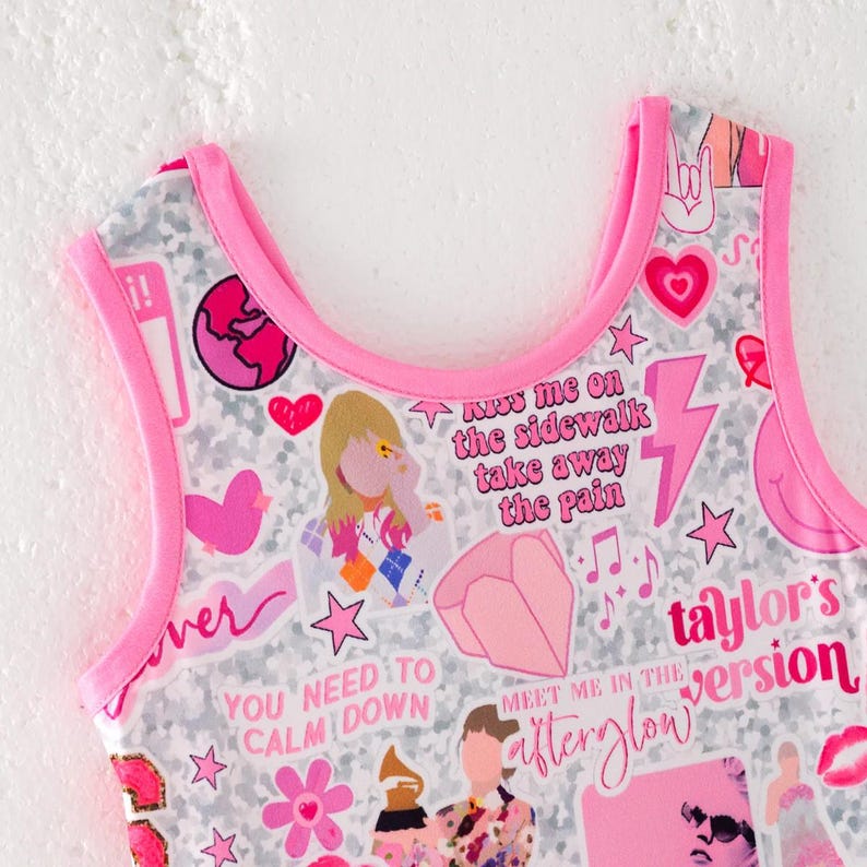 May include: A sleeveless top with a bright pink trim featuring a white and gray patterned background covered in various pink and colorful stickers, including text that reads Kiss me on the sidewalk take away the pain, You need to calm down, and Taylor's version.