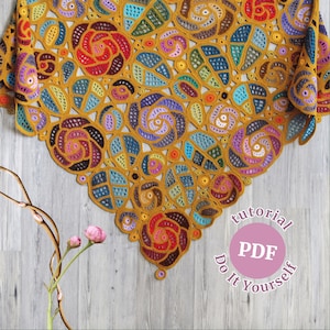 May include: A crocheted shawl with a colorful floral pattern in shades of yellow, orange, red, blue, green, and purple. The shawl is made with a delicate openwork stitch and has a scalloped edge. The text "tutorial PDF Do It Yourself" is printed on a pink circle.