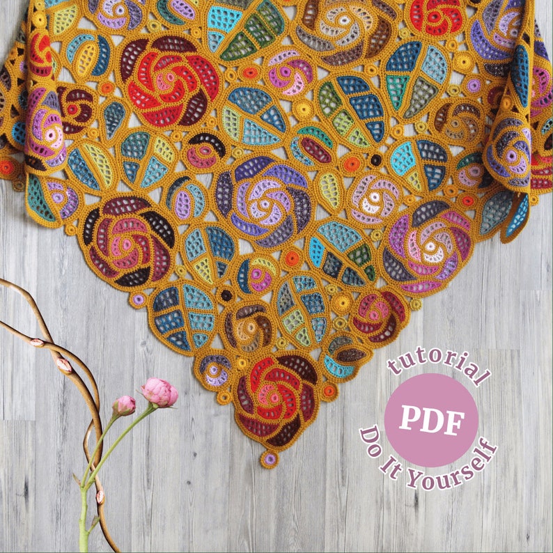May include: A crocheted shawl with a colorful floral pattern in shades of yellow, orange, red, blue, green, and purple. The shawl is made with a delicate openwork stitch and has a scalloped edge. The text "tutorial PDF Do It Yourself" is printed on a pink circle.