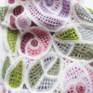 May include: A white crocheted doily with a circular design featuring various colors, including pink, purple, green, and gray.