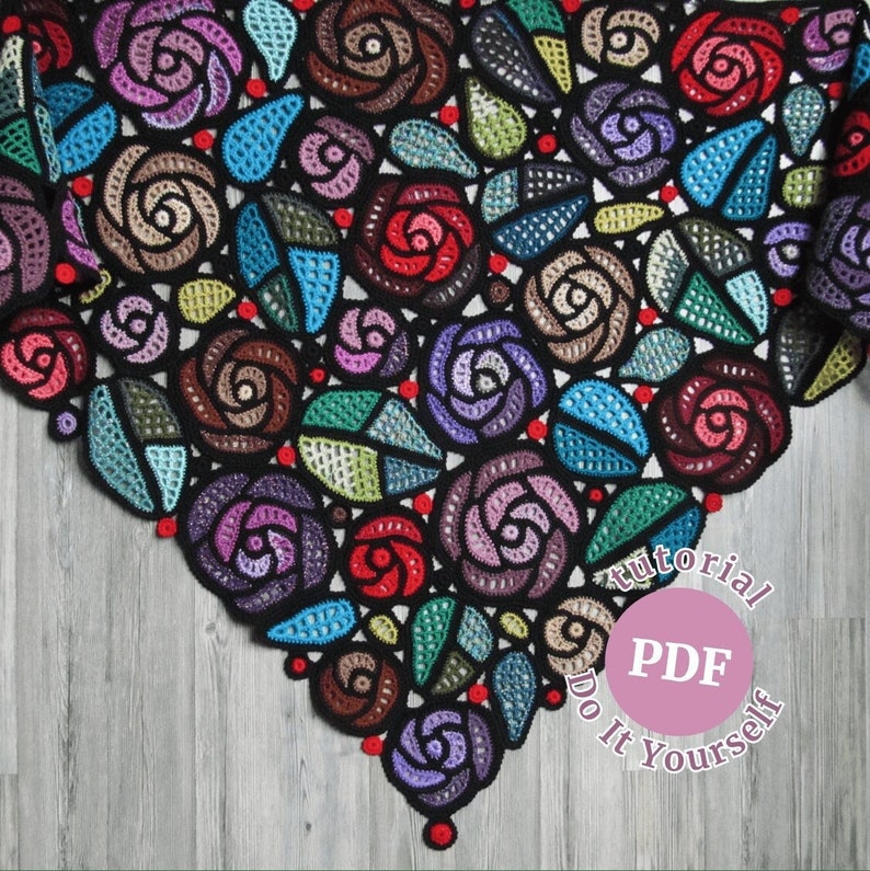 May include: A black crochet shawl with a design of colorful roses. The shawl is on a wooden surface. The text "Tutorial PDF Do It Yourself" is on a pink circle.
