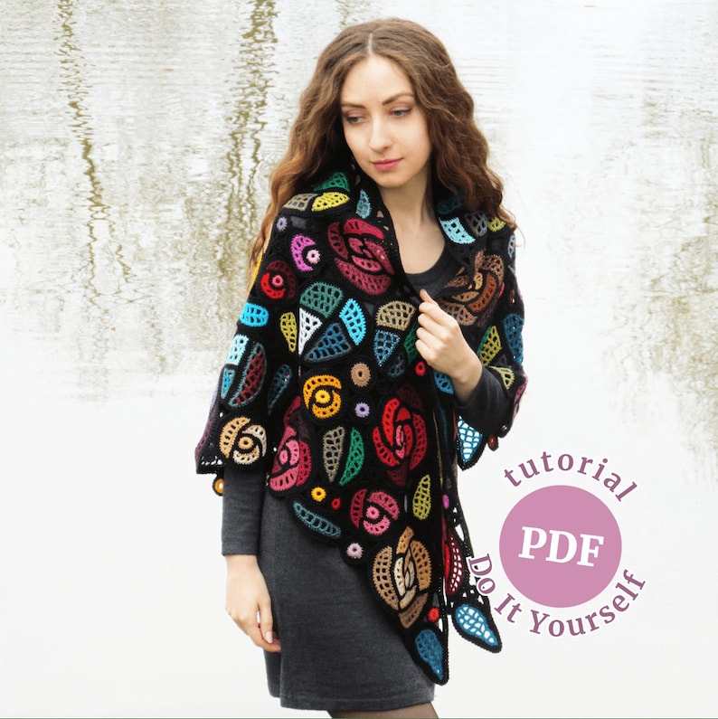 May include: A black crochet shawl with colorful floral designs. The shawl is worn by a person with long brown hair. The text "tutorial PDF Do It Yourself" is on a pink circle.