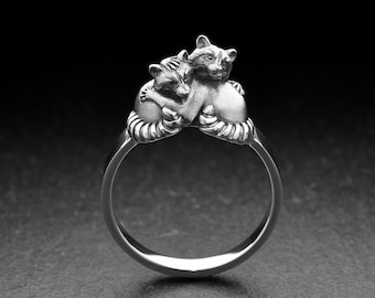 May include: A silver ring with two cats curled up together. The cats are detailed and realistic.