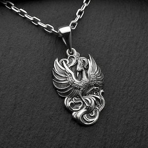 Pu&ograve; includere: Una collana con un ciondolo in argento che presenta un design dettagliato e ornato di una fenice con le ali spiegate. La fenice &egrave; raffigurata in uno stile classico e mitologico, con dettagli intricati nelle sue piume e nel suo corpo.