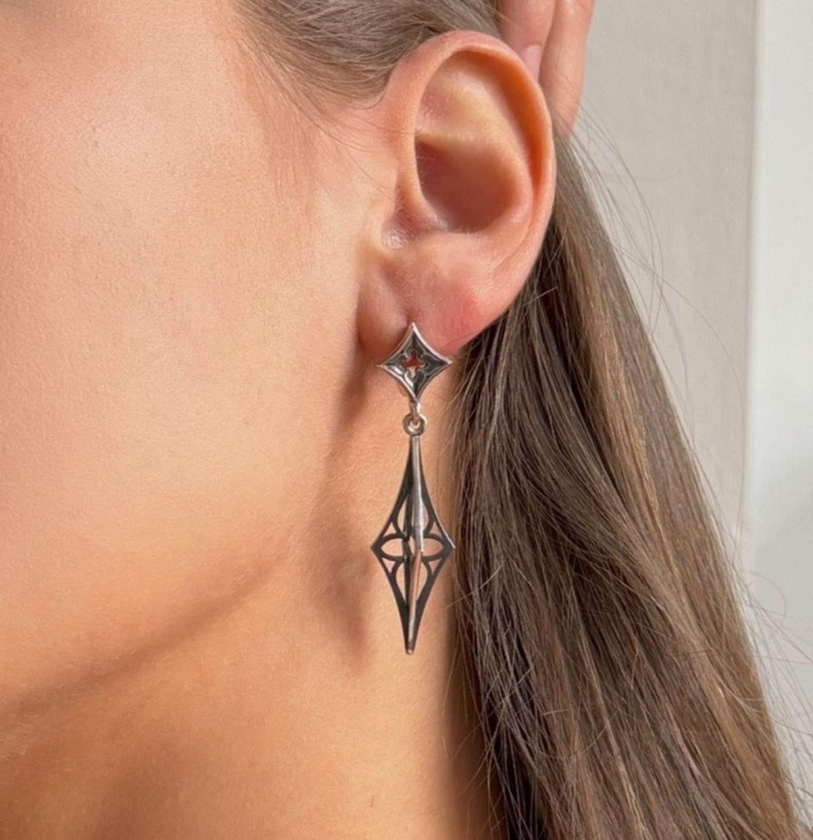 Sterling silver cathedral dagger earrings worn on ear, showcasing elegant gothic drop design