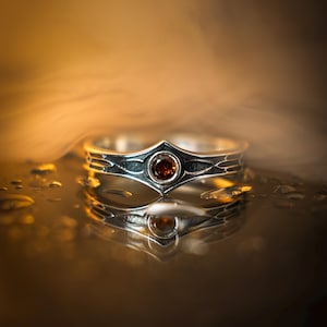 Sterling Silver Garnet Ring with Ornate Etching, Gothic Bloodstone-Inspired Statement Band for Men or Women, Red Gem Warrior Ring, This angle emphasizes the smooth, bezel setting of the stone—a practical choice for a "Warrior" ring as it prevents snagging during action. The 925 sterling silver has a satin finish on the high points and a matte black finish in the recessed grooves. The stone has high clarity, catching the light and appearing to glow from within against the cool grey metal.