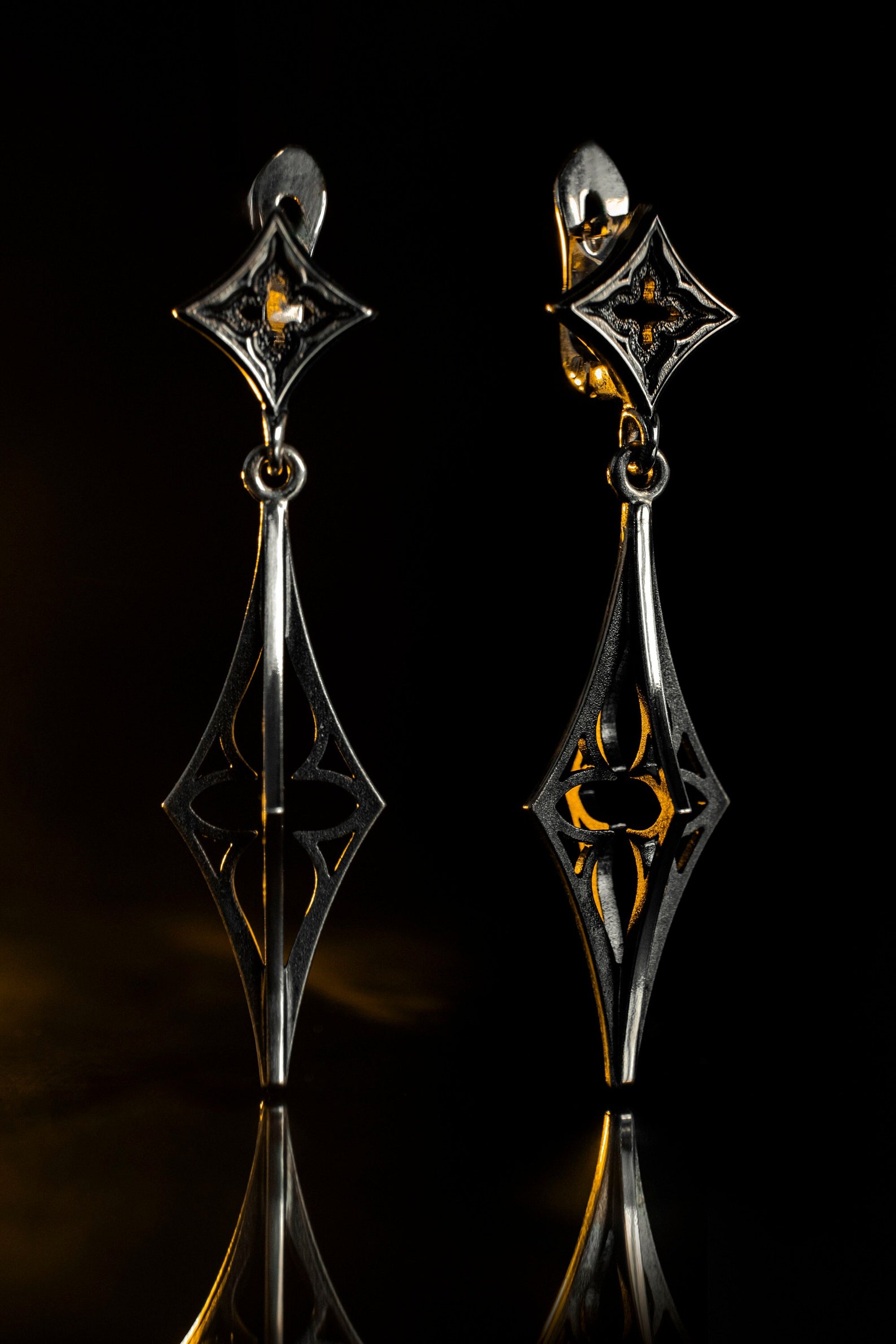 Gothic silver earrings glowing under moody lighting, showcasing the dark oxidized finish