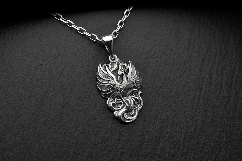 Pu&ograve; includere: Una collana con un ciondolo in argento che presenta un design dettagliato e ornato di una fenice con le ali spiegate. La fenice &egrave; raffigurata in uno stile classico e mitologico, con dettagli intricati nelle sue piume e nel suo corpo.