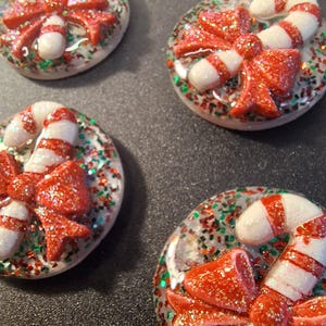 May include: Four Christmas-themed resin ornaments. Each ornament features a red glittery bow and a white and red candy cane. The ornaments are round and embedded with red, green, and silver glitter.