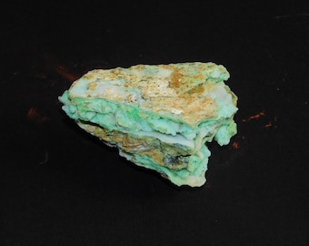 May include: A rough-hewn, layered rock formation with a striking color palette. The rock features a vibrant, light green hue interspersed with areas of tan and brown. The overall texture appears coarse and natural, suggesting a mineral specimen.