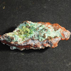May include: A rough, irregularly shaped rock with a mix of green, white, and orange colors. The rock has a rough, textured surface.