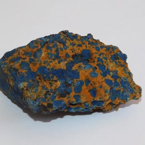 Pode incluir: Uma rocha texturizada com uma mistura de tons azuis e laranja. O azul está concentrado em pequenas manchas irregulares, enquanto o laranja preenche os espaços. A rocha tem uma aparência natural e não polida.