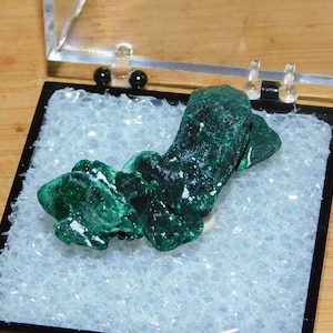 May include: A green malachite mineral specimen in a clear plastic display case with a white foam interior.