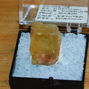 May include: A yellow fluorite crystal with red inclusions in a small black display box. The label reads "Fluorite, El Hammam Mine, Khemisset, Prov. Rabat, Sale - Kenitra Reg., Morocco".