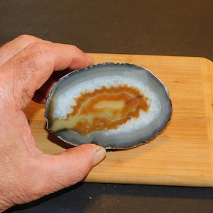 May include: A polished agate slice with a brown and white banded pattern. The agate is translucent and has a smooth, polished surface.