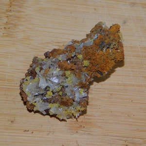 May include: A cluster of white crystals with yellow accents on a brown, rough, rock-like surface.