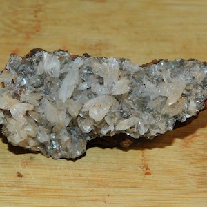 Puede incluir: Un cúmulo de cristales blancos translúcidos sobre una roca gris oscura. Los cristales están dispuestos en un patrón aleatorio y tienen un ligero brillo iridiscente.