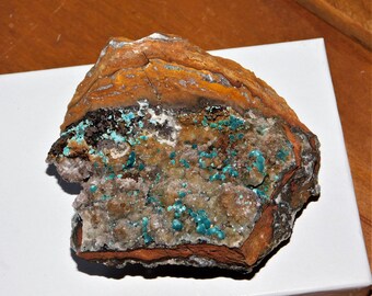 May include: A raw mineral specimen featuring a thick, layered, rusty-orange and brown outer crust surrounding a central cavity filled with small, vibrant turquoise-blue crystalline clusters and textured, earthy brown mineral deposits.