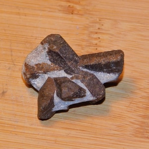 Puede incluir: Un grupo de cristales marrones y grises con una textura rugosa y natural. Los cristales están dispuestos en forma de estrella.