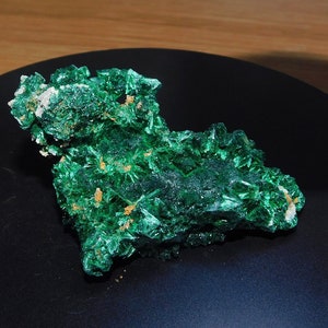 May include: A large, green malachite crystal cluster with a rough, textured surface. The crystal is a vibrant green color with a slight sheen.