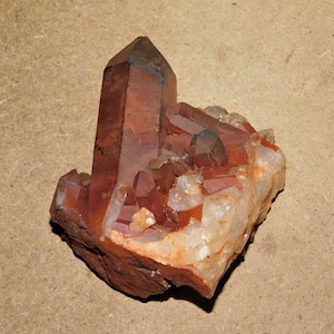 May include: A cluster of red and clear quartz crystals on a rough, brown rock. The crystals are pointed and have a natural, raw appearance.