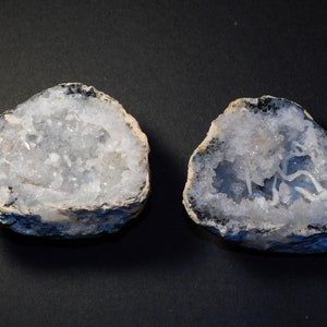 Op de afbeelding: Twee helften van een geode met witte kristalformaties erin. De buitenkant van de geode is donkergrijs.