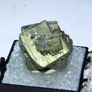 Puede incluir: Un cristal de pirita verde con brillo metálico, exhibido en una pequeña caja negra con acolchado de espuma blanca.