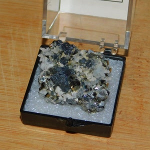 May include: A small collection of black and silver pyrite and hematite crystals in a black display case with a white background.